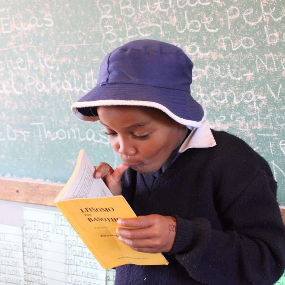 A young student in school uniform reads a Sesotho storybook