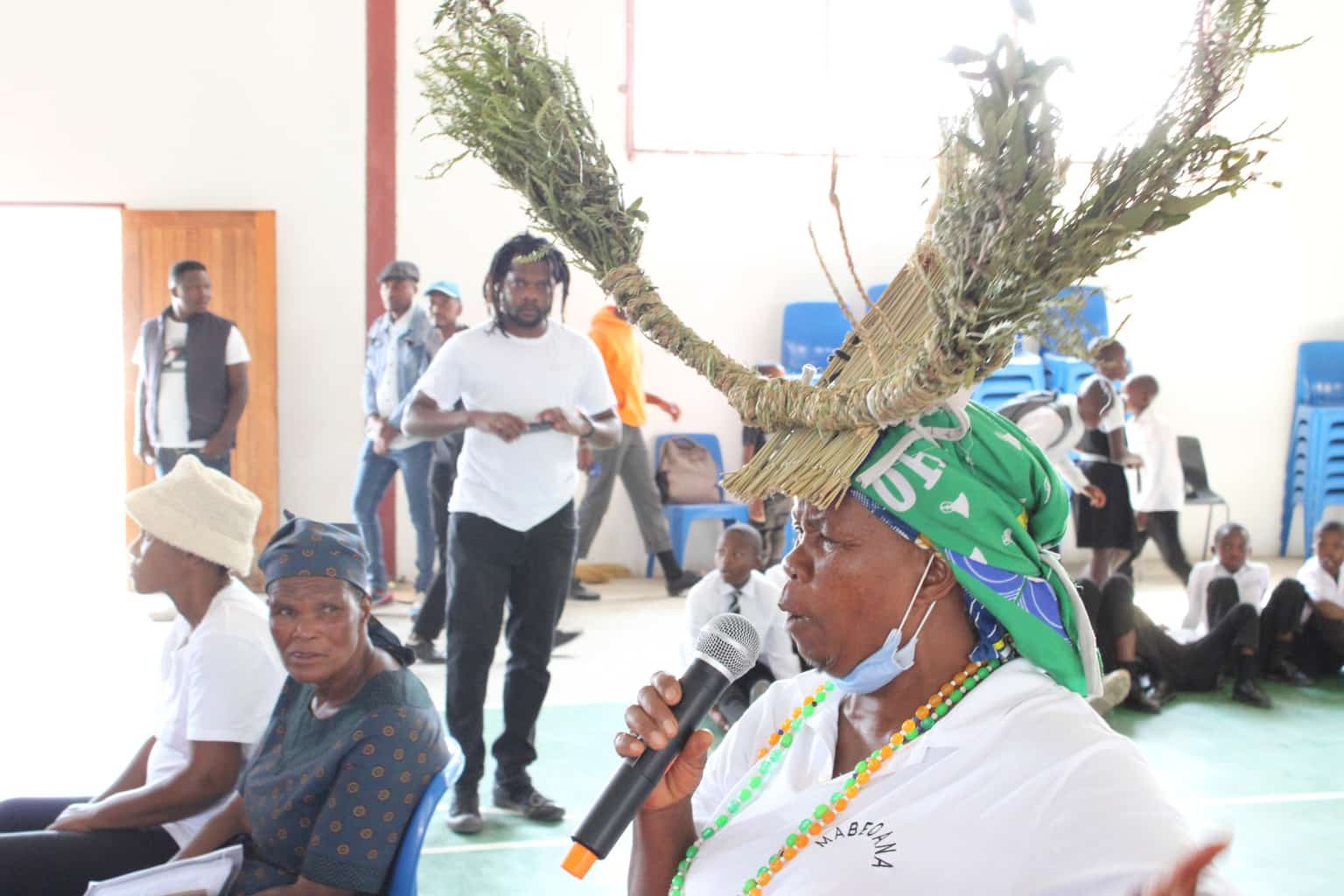 A community elder wearing a traditional headdress speaks at a gathering