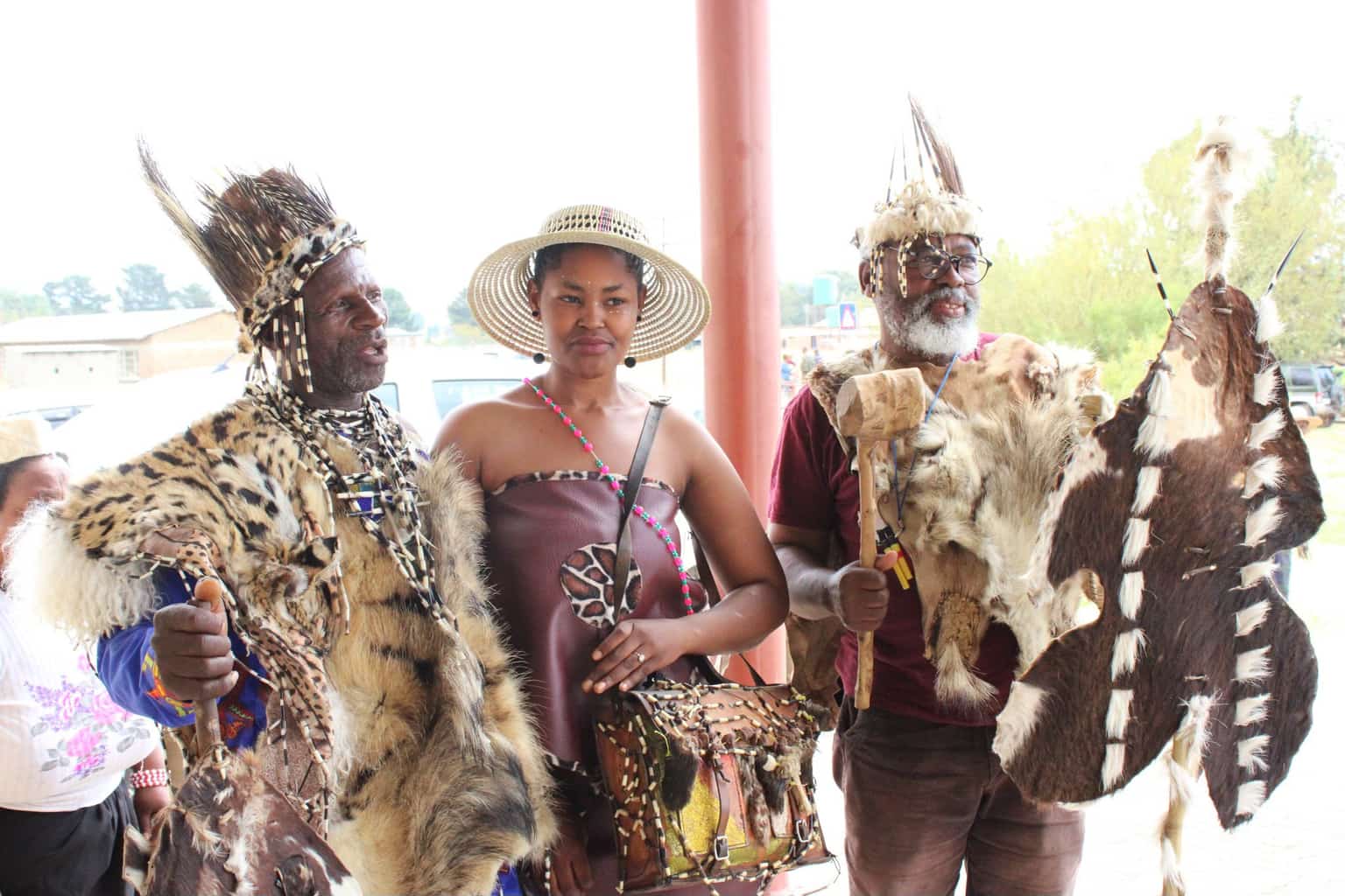 Three people in traditional Basotho ceremonial attire with leopard skins and feathered headdresses